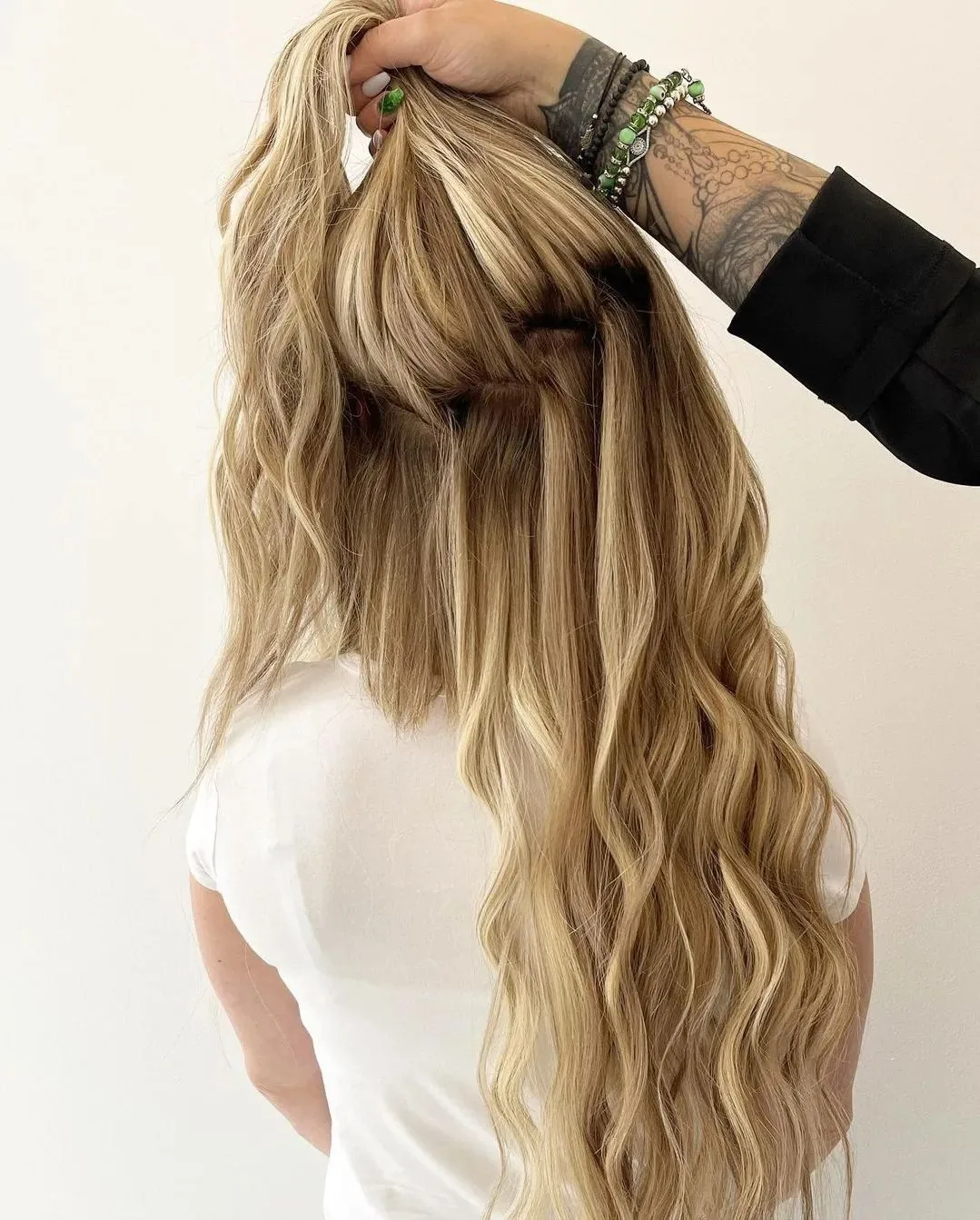 A section of long blonde wavy hair lifted at the crown to show the extension attachment area &mdash; Monaco Salon Tampa
